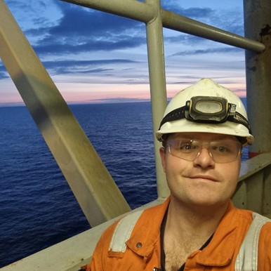 james gammon on an oil rig offshore in safety gear and in front of a sunset